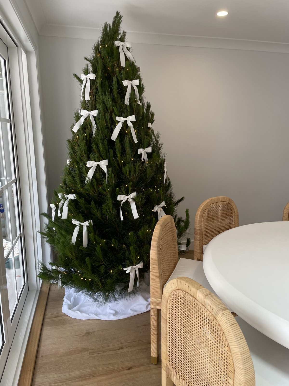 Real Christmas tree decorated with classic white bows beside a dining table
